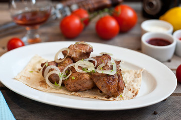 Meat kebab with onions on a white plate on a wooden background. Grilled meat