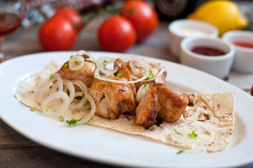 Meat kebab with onions on a white plate on a wooden background. Grilled meat