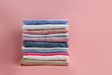 Stack of colorful perfectly folded clothing items. Pile of different pastel color shirts and sweaters isolated on pale pink background. Close up, copy space.