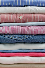 Fototapeta na wymiar Cropped image with stack of colorful perfectly folded clothing items. Macro shot of pile of different pastel color shirts, sweaters & pants. Close up, copy space, background.