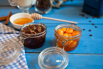 Various glass vases with fruit jams tangerine, walnut and honey on a blue wooden background.