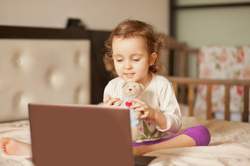 Little cute girl sitting on the bed and using a digital tablet laptop notebook. Online call friends or parents.