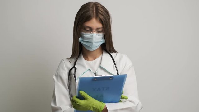 Doctor in a medical gown shows a folder with the text stay at home