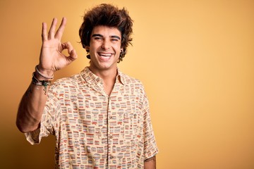 Young handsome man on vacation wearing summer shirt over isolated yellow background smiling positive doing ok sign with hand and fingers. Successful expression.