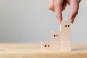 Hand arranging wood block stacking as step stair on top with word Step By Step. Business concept for personal ladder of success process