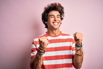 Young handsome man wearing striped casual t-shirt standing over isolated pink background excited for success with arms raised and eyes closed celebrating victory smiling. Winner concept.