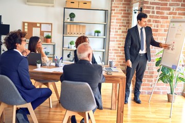 Group of business workers smiling happy and confident in a meeting. Working together looking at presentation using board and charts at the office.