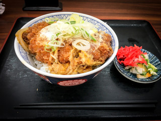 Katsudon, a bowl of rice topped with a deep-fried pork cutlet, egg, vegetables, and condiments, with Tsukemono pickles on the table in local restaurant in Japan.