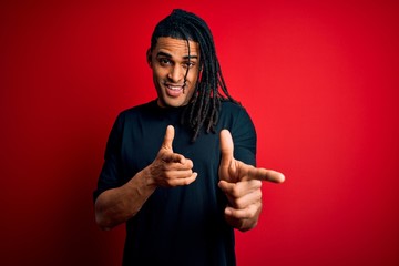 Young handsome african american afro man with dreadlocks wearing casual t-shirt pointing fingers to camera with happy and funny face. Good energy and vibes.
