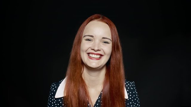 Close up of a young woman laughing. Cheerful woman with long brown hair isolated on black background.
