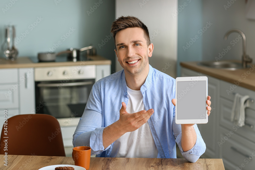 Sticker Handsome man with tablet computer in kitchen at home