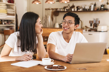 Image of multicultural couple making notes in planner and using laptop