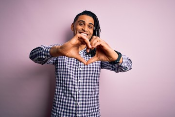 Young handsome african american afro man with dreadlocks wearing casual shirt smiling in love doing heart symbol shape with hands. Romantic concept.