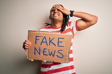 Young african american man with dreadlocks holding banner with fake news message protest stressed...