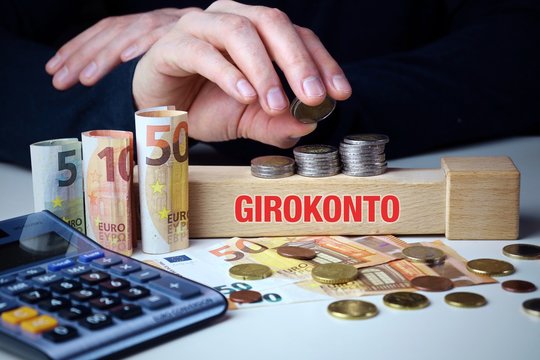 Girokonto. M&auml;nnliche Hand stapelt Geld-Turm (Euro). Begriff an Baustein. M&uuml;nzen, Scheine & Taschenrechner. Konzept f&uuml;r Business, Finanzen, Statistik