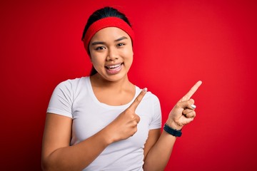 Young beautiful asian sporty woman wearing sportswear doing sport over red background smiling and looking at the camera pointing with two hands and fingers to the side.