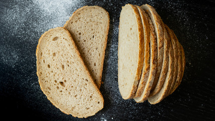 Sliced bread on a black background. Slices of bread and scattered flour. Bread and flour