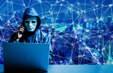 Anonymous computer hacker in white mask and hoodie. Obscured dark face using laptop computer for...