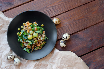 Warm salad of fried mushrooms, green peas, carrots and arugula, top view. Served with grapes and quail eggs