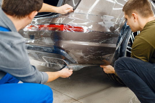 Two workers applies car protection film on bumper