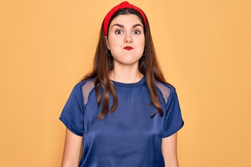 Young beautiful brunette woman wearing red lips over yellow background puffing cheeks with funny face. Mouth inflated with air, crazy expression.