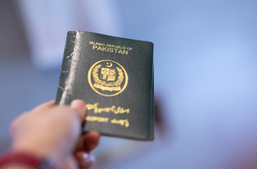 A hand holds passport of Pakistan. Focus on letters on the passport. 