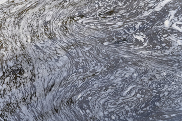 Water in a river pool forming natural patterns of foam.