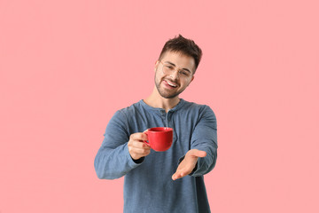 Young man with cup of hot coffee on color background