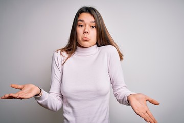 Young beautiful brunette girl wearing casual sweater standing over isolated white background...