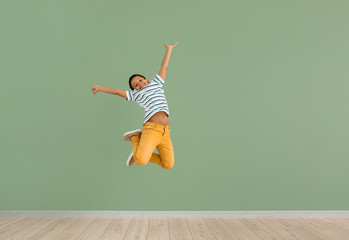 Little African-American boy jumping against color wall