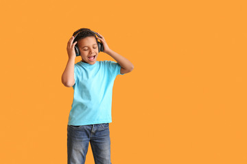 Little African-American boy listening to music against color background
