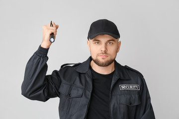 Male security guard with flashlight on grey background