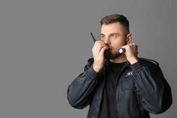 Male security guard with flashlight on grey background