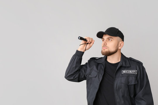 Male security guard with flashlight on grey background