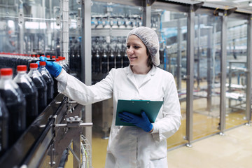 Young happy female worker in bottling factory checking juice bottles before shipment. Inspection quality control.