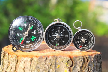 Three different classic navigational compass on stump in summer on natural background