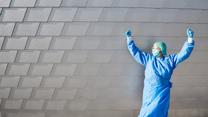 Doctor cheers with clenched fists in front of clinic in protective clothing