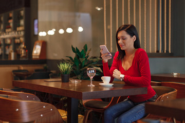 Beautiful young woman suing smartphone and drinking coffee in a cafe