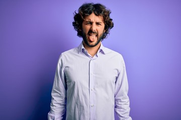 Fototapeta na wymiar Young handsome business man with beard wearing shirt standing over purple background sticking tongue out happy with funny expression. Emotion concept.