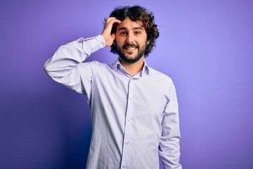 Young handsome business man with beard wearing shirt standing over purple background smiling confident touching hair with hand up gesture, posing attractive and fashionable