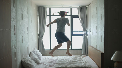 Handsome man have fun, jumping, dancing on bed by the window