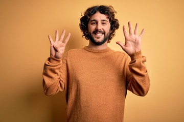 Young handsome man with beard wearing casual sweater standing over yellow background showing and...