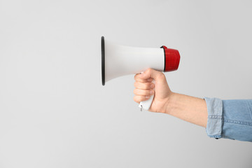 Male hand with megaphone on light background