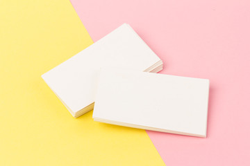 Obraz na płótnie Canvas white blank business cards on pink and yellow background in close-up