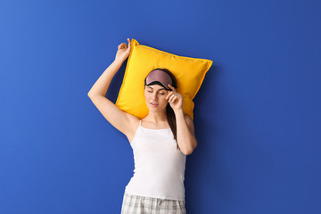Young woman in sleep mask and with pillow on color background