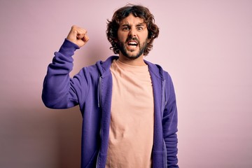 Young handsome sporty man with beard wearing casual sweatshirt over pink background angry and mad...