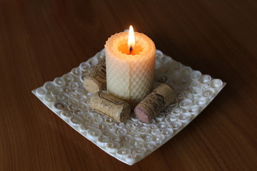 Burning white candle on the plate made of seashells with three wine corkes