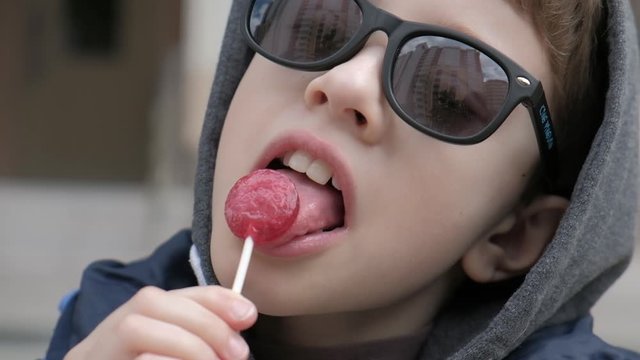 Boy sitting on a bench and eats Lollipop. Rejoices licks the candy, fools around