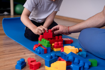 The boy sits on the floor and plays with the designer, sitting next to the man and helps the guy to put a tower, concept development of children