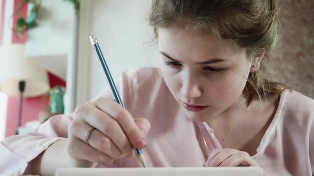 Face of concentrated teenaged blond with pencil. She draws a picture. Artist's hobby and leisure.